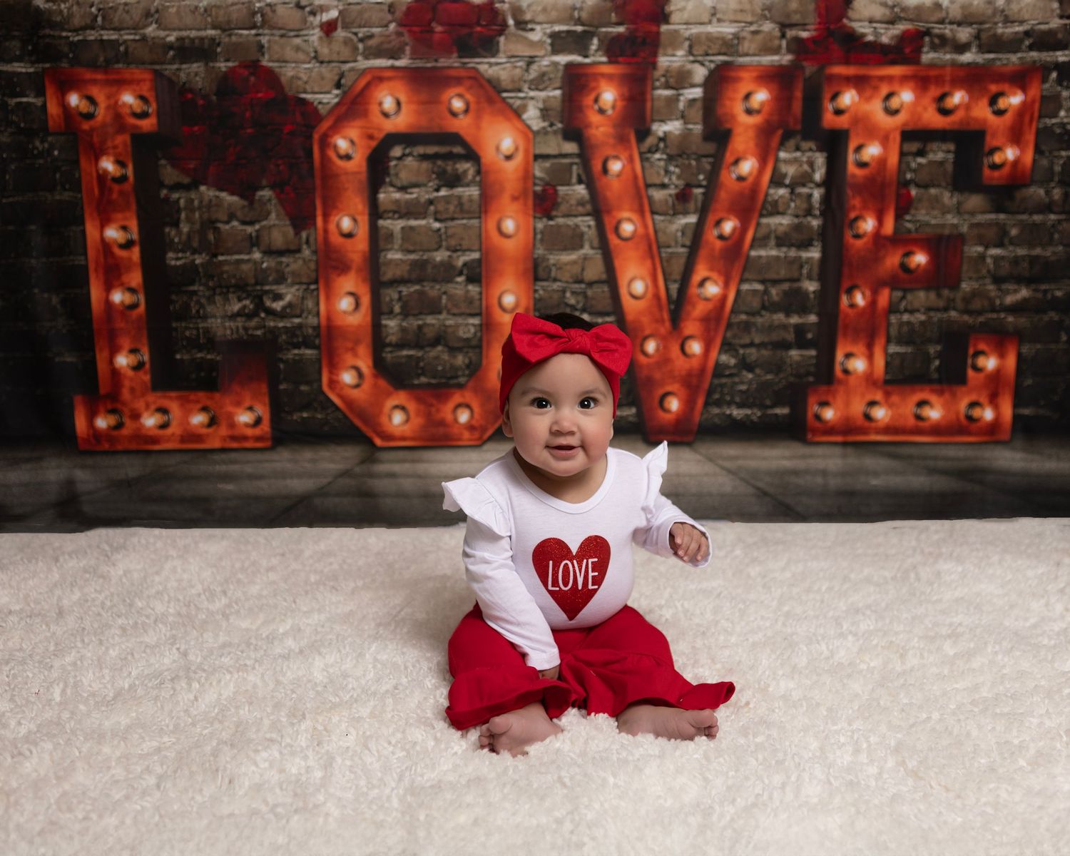Red illuminated love sign with brick wall background and person posing in red outfit.