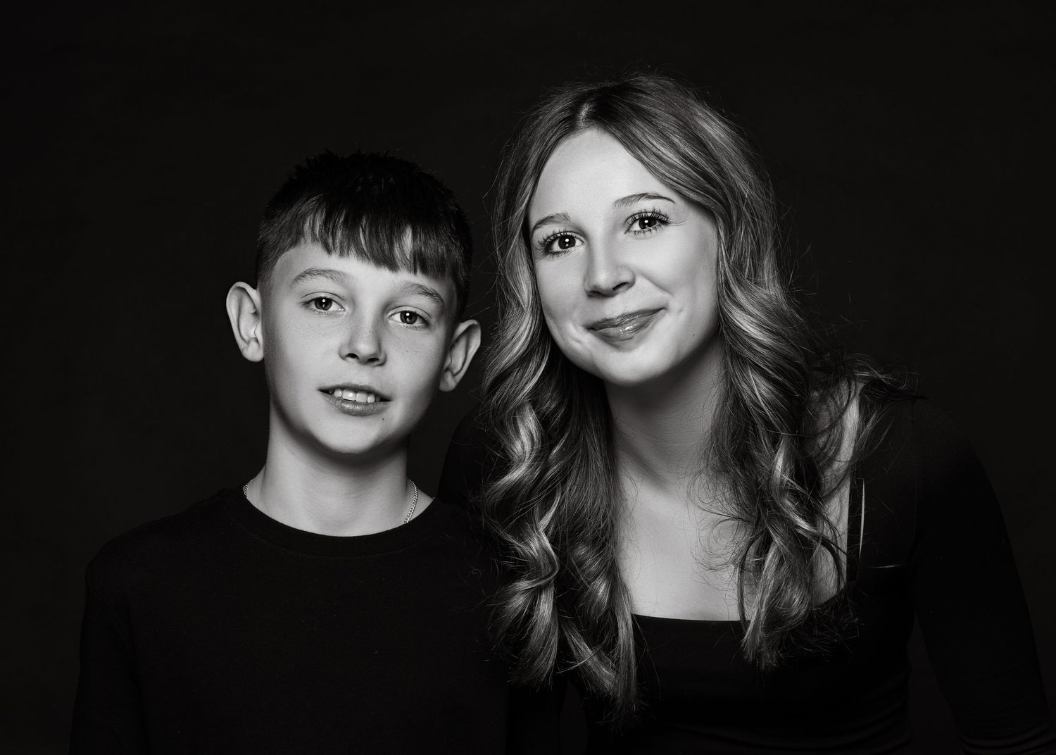 Black and white portrait of two close family members posing together against a dark backdrop.