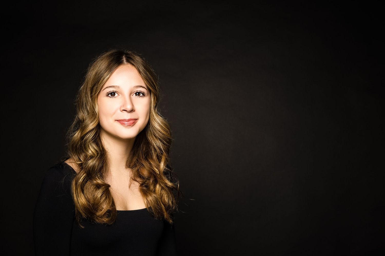 Professional portrait against dark background showing wavy blonde hair and black top with natural smile.