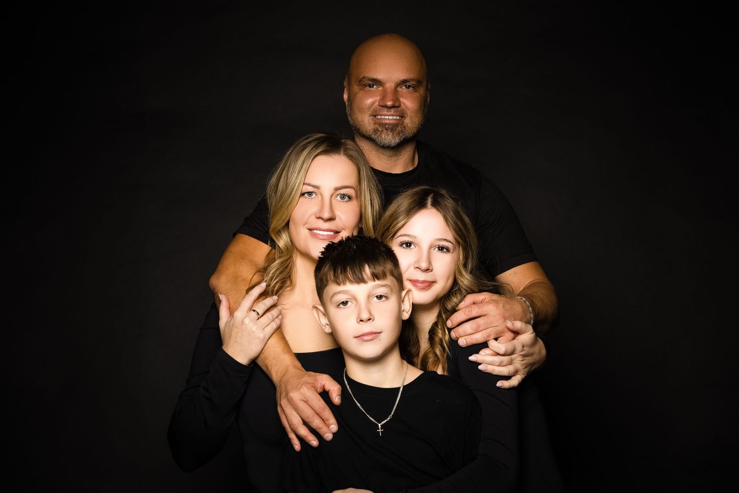 Color studio portrait of a family of four embracing against a dark background.