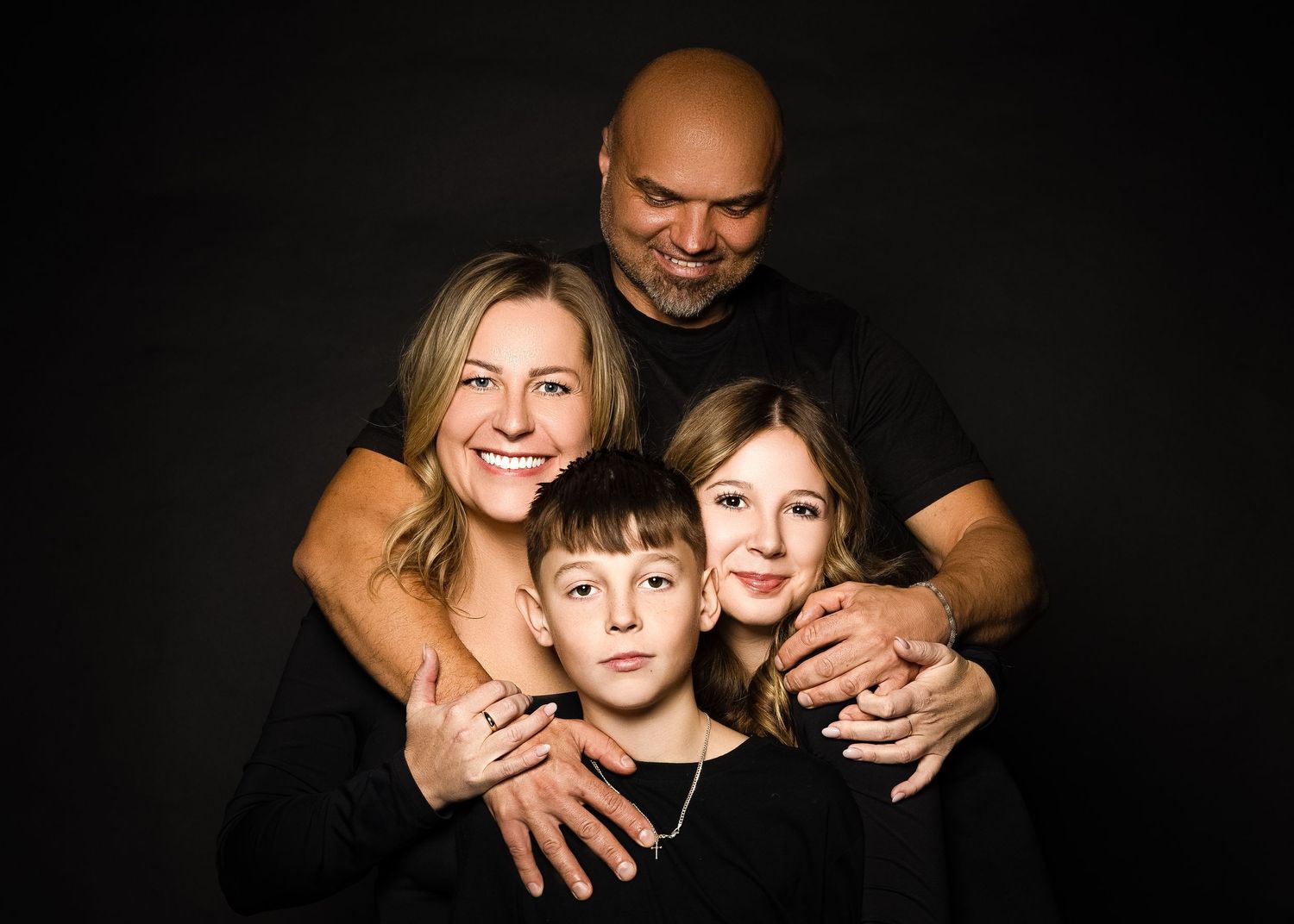 Portrait of a smiling family of four posed together against a dark background.