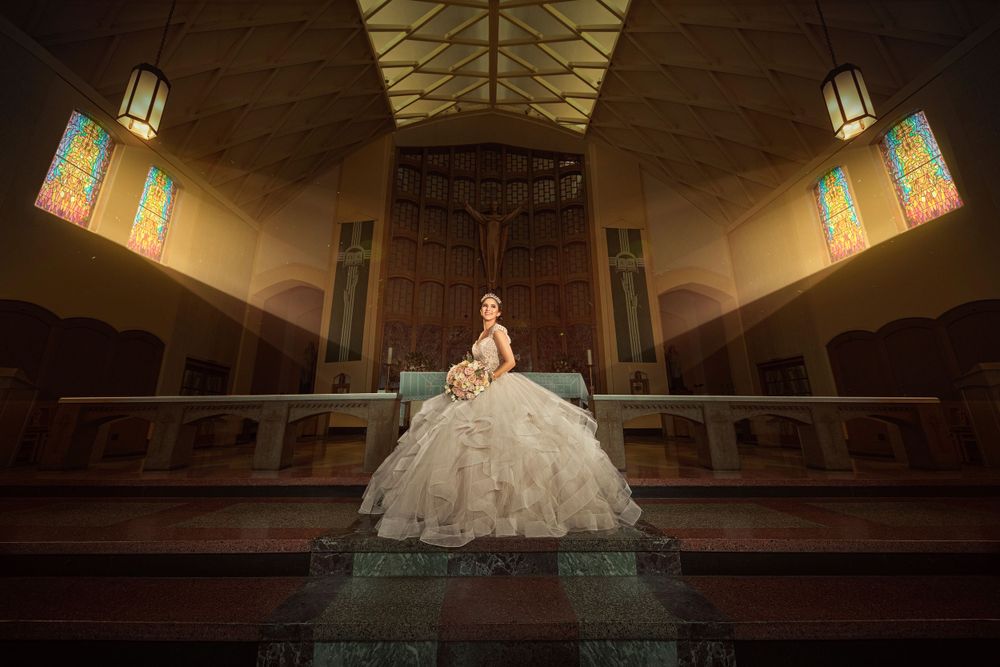 A dramatic portrait in an ornate church interior features a flowing white formal gown against stained glass windows.