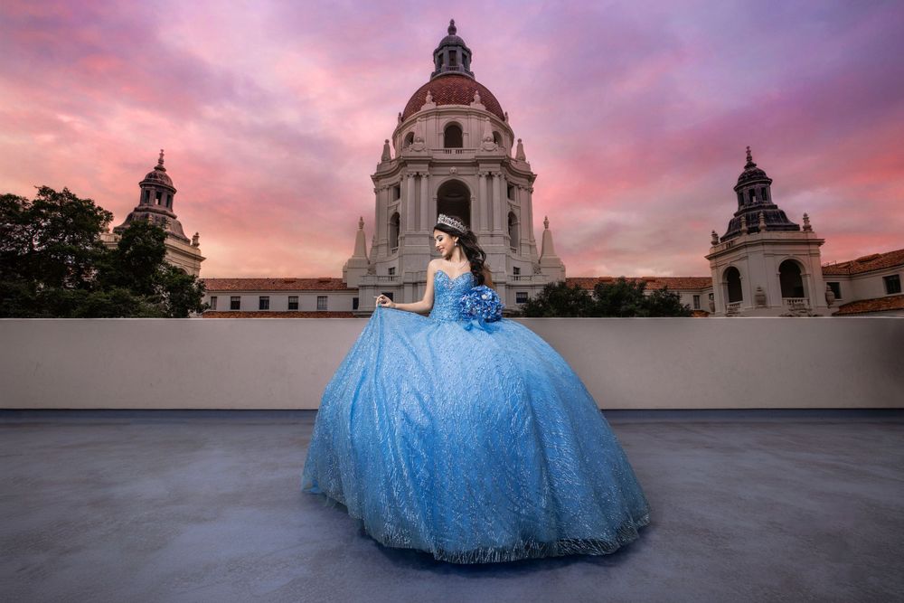 A flowing blue ball gown dress photographed in front of Pasadena City Hall during a dramatic pink sunset.