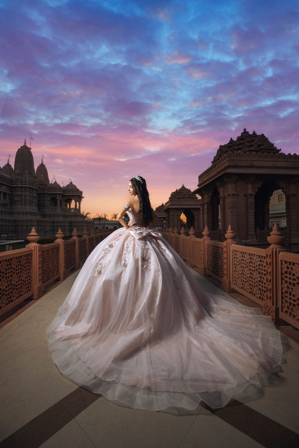 A dramatic photo of a flowing white gown on an ornate temple bridge at sunset with pink and purple clouds.