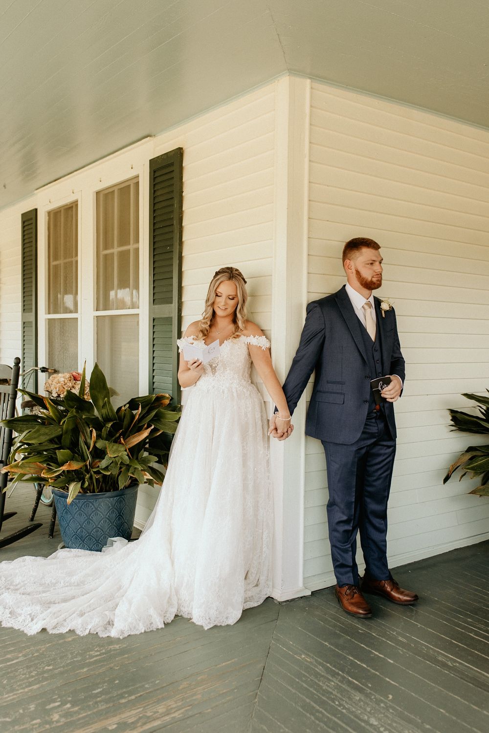 Photograph of a wedding couple holding hands on white farmhouse porch with potted plants at Wild Daisy Farm in Molena, Georgia.