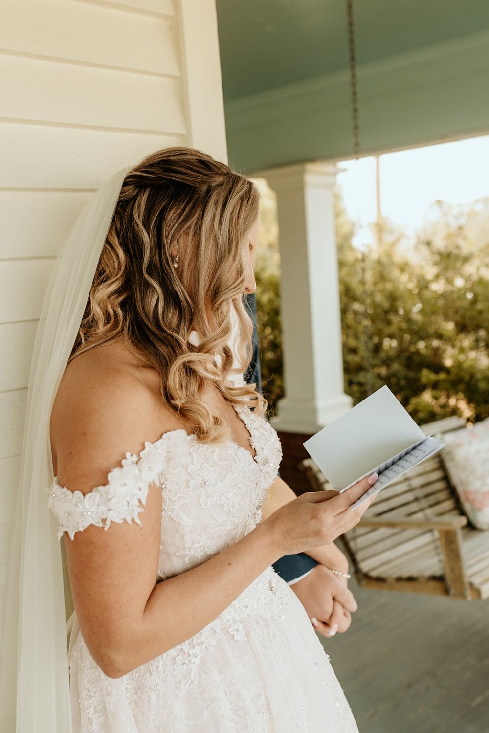 Photograph of Bride in lace gown reading letter on rustic farmhouse porch at wild daisy farm in molena, georgia