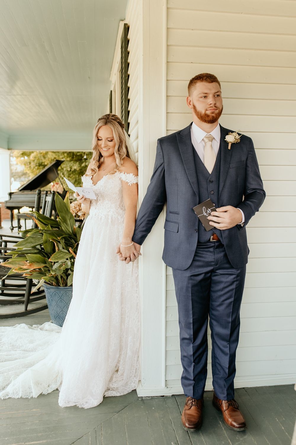 Photograph of a couple standing in first look pose on gray farmhouse porch at Wild Daisy Farm in Molena, Georgia.