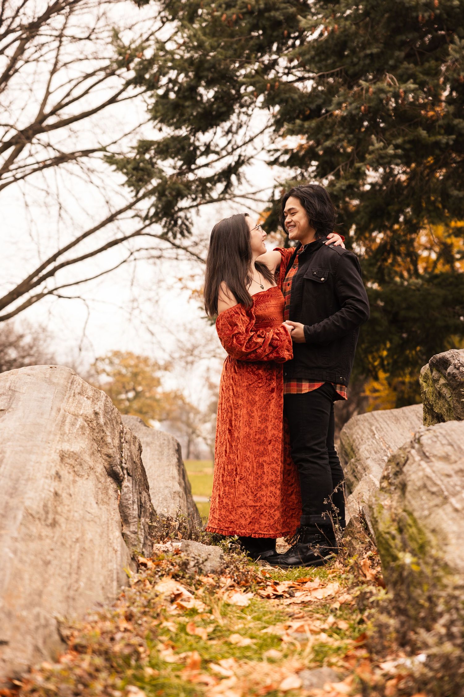 A romantic couple poses on rocky terrain surrounded by autumn trees.