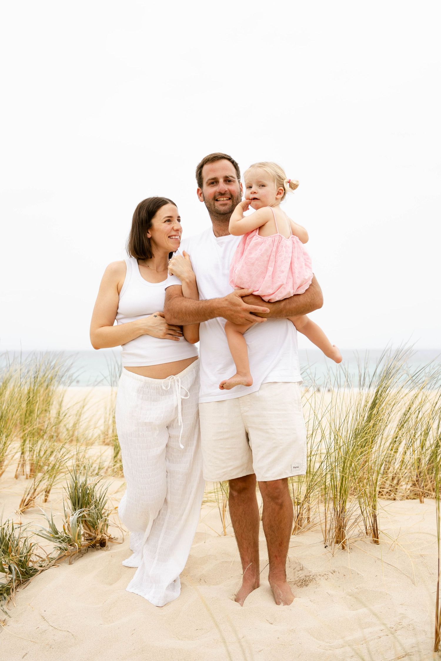 Family portrait on beach with dune grass, all dressed in white casual clothing.