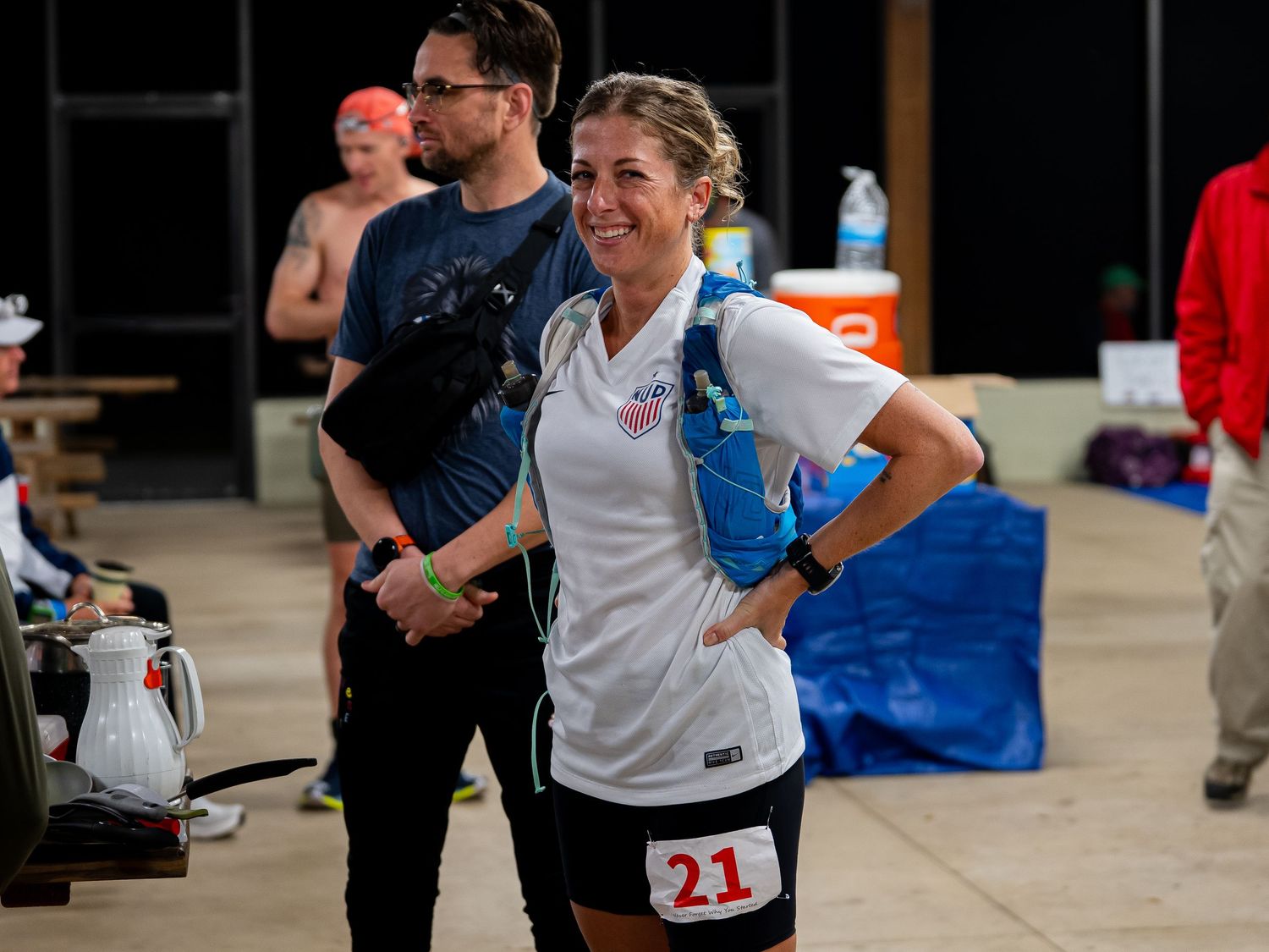 Runner with bib number 21 smiling at indoor event checkpoint or aid station.