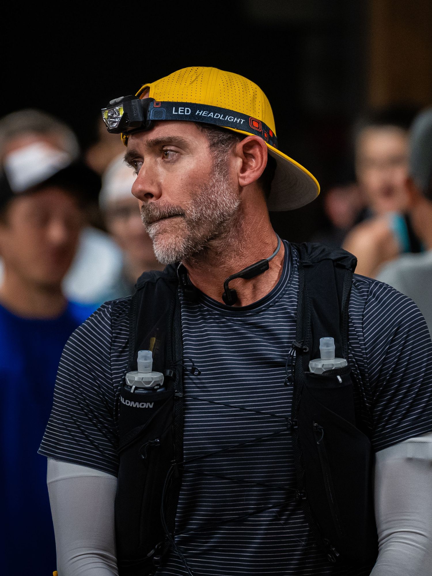 Trail runner wearing yellow LED headlamp cap and striped shirt at outdoor event.