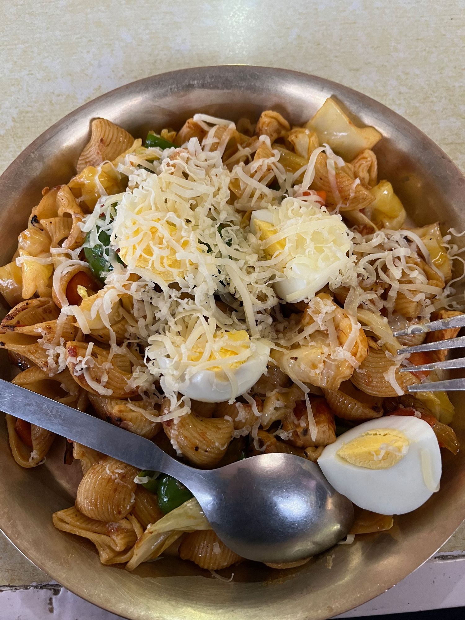 Pasta dish topped with shredded cheese and sliced boiled eggs on a metal serving platter.