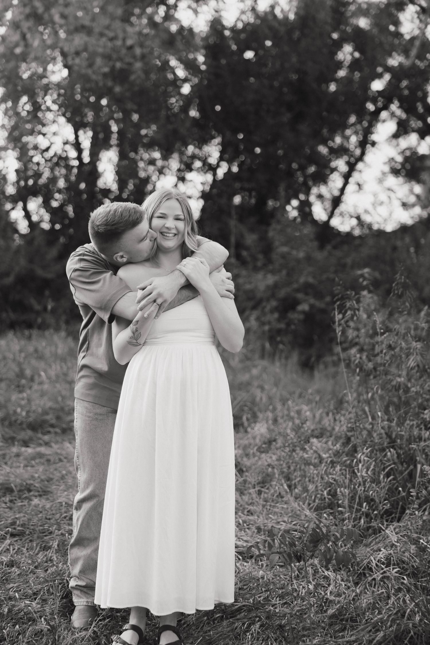 A couple embraces in a romantic moment on a grassy hillside in black and white.