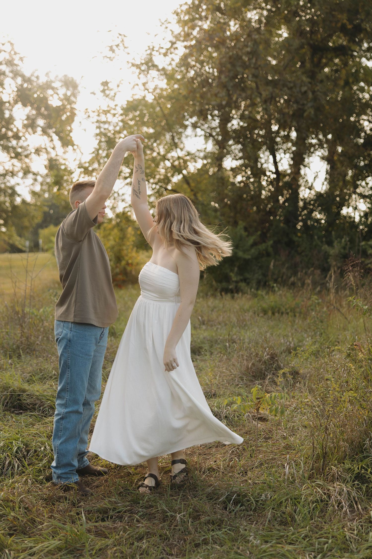 A couple dances joyfully together in a sunlit meadow with tall grass at golden hour.