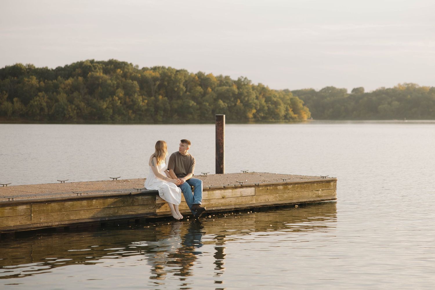 Two people sitting together and enjoying a peaceful moment by the dock on a serene lake at sunset.