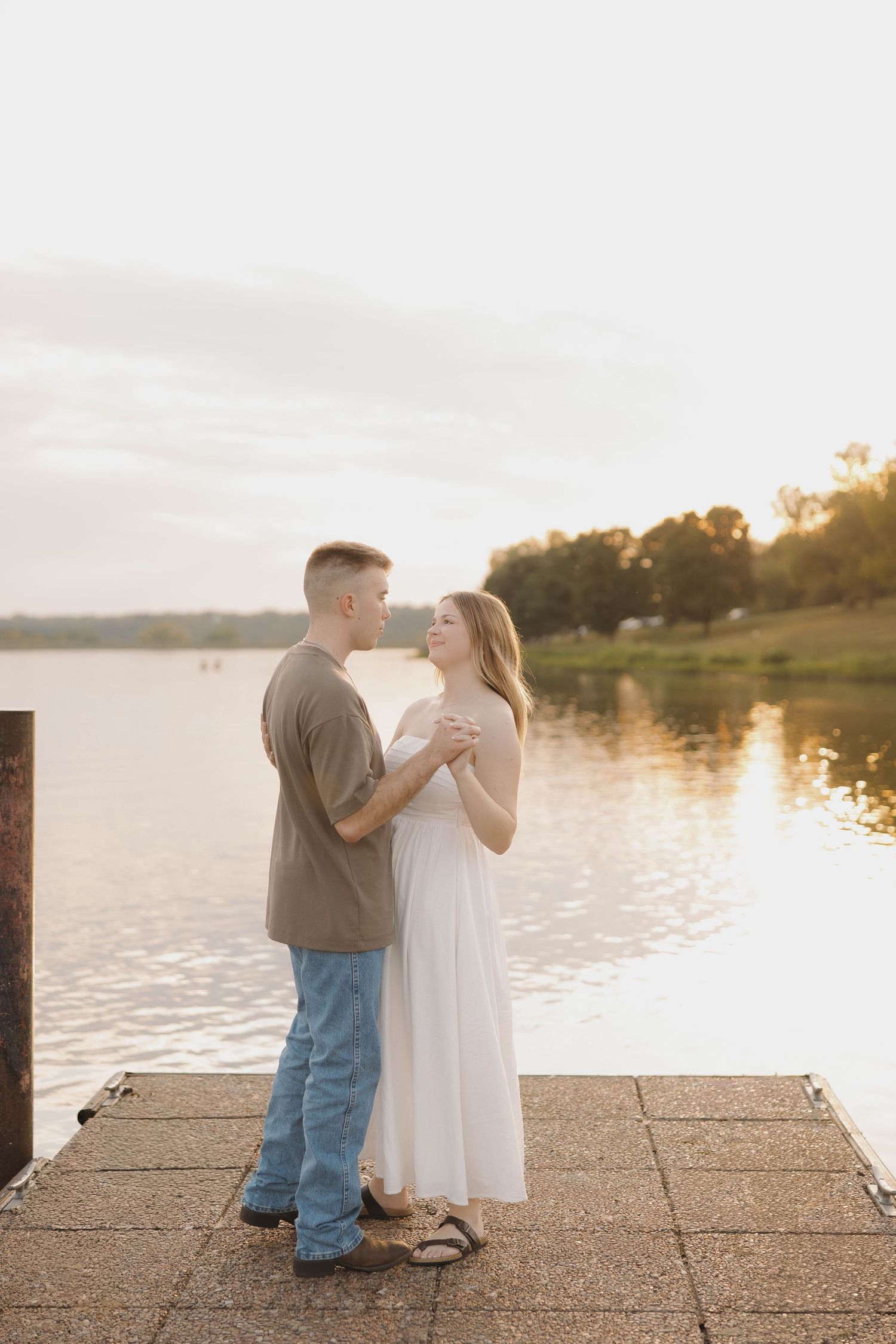 A couple shares a tender moment at sunset on a lakeside dock.