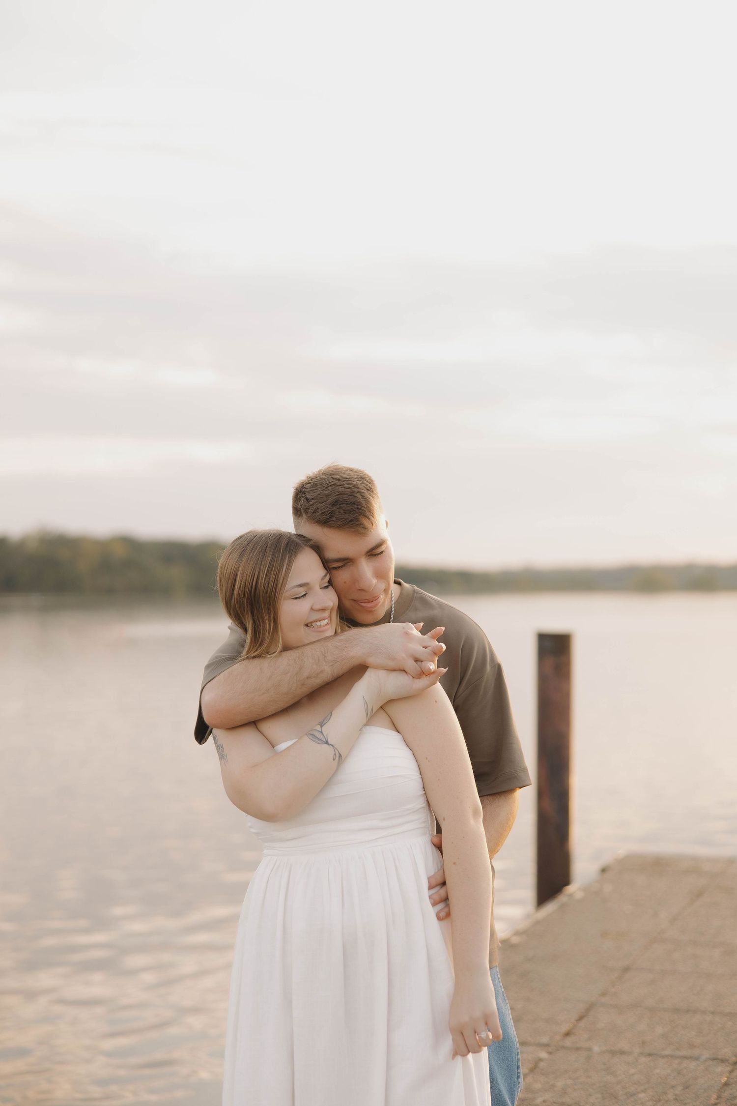 A loving couple shares an intimate embrace while standing on a lakeside dock during golden hour.