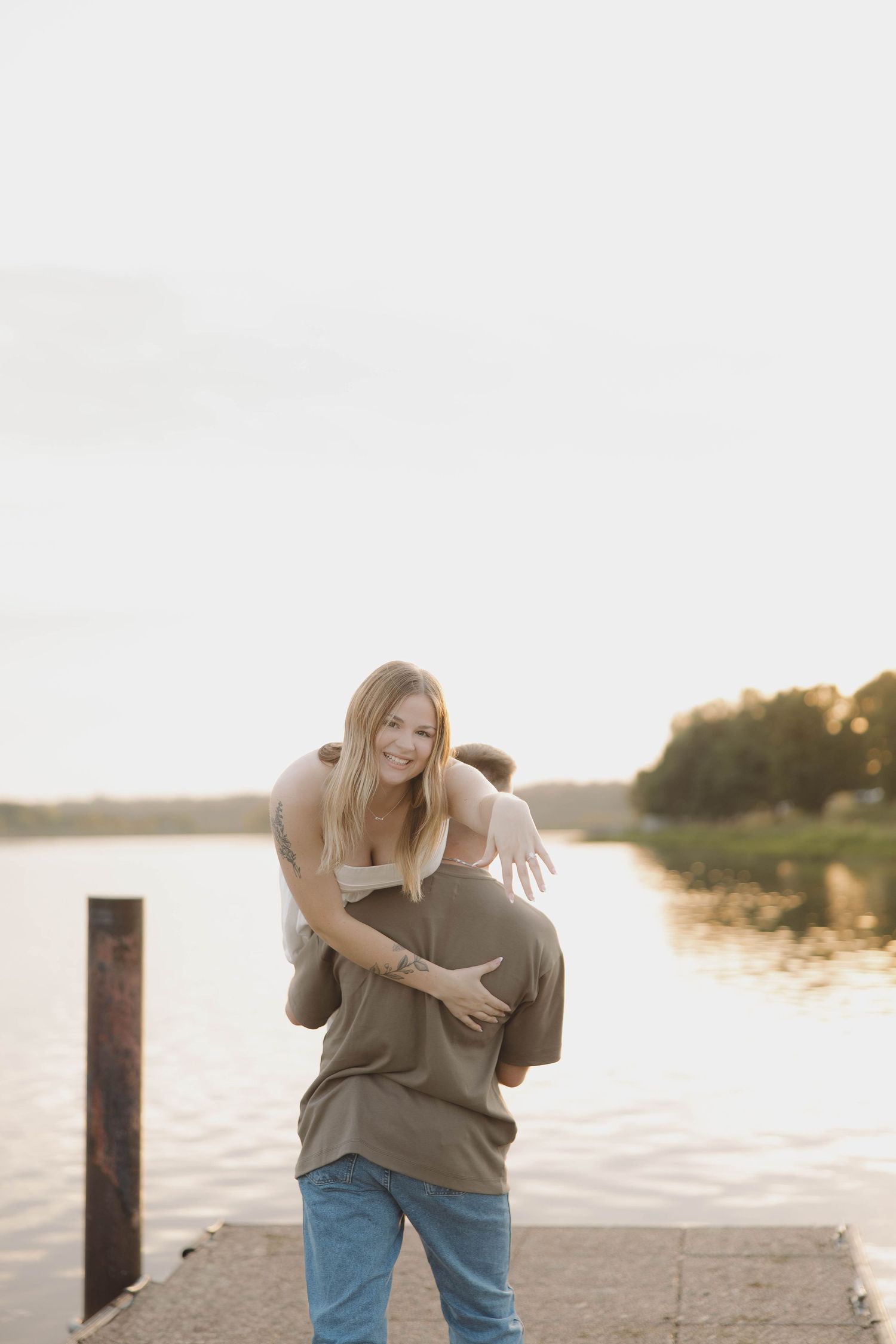A joyful moment of a couple playing and laughing together by the waterfront at sunset.