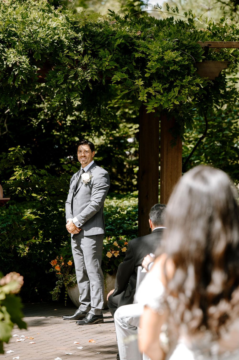 Sequence of playful moments near lush green hedges showing a person in a light gray suit jumping.