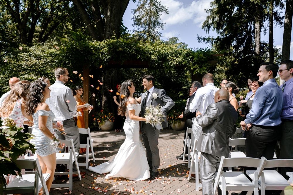 Wedding guests gathered outdoors in a garden setting celebrate during a daytime summer ceremony.