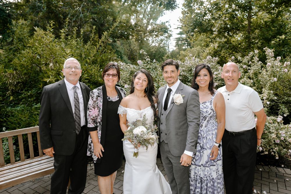Wedding guests gather outdoors on a sunny afternoon surrounded by green foliage.