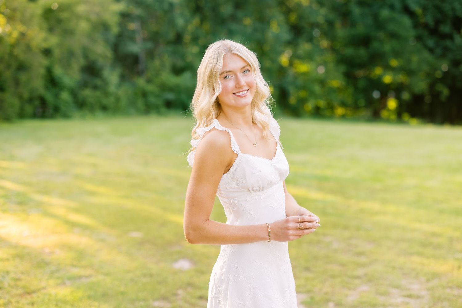 A person wearing a white dress stands outdoors in a sunlit field during sunset with glowing golden backlight.