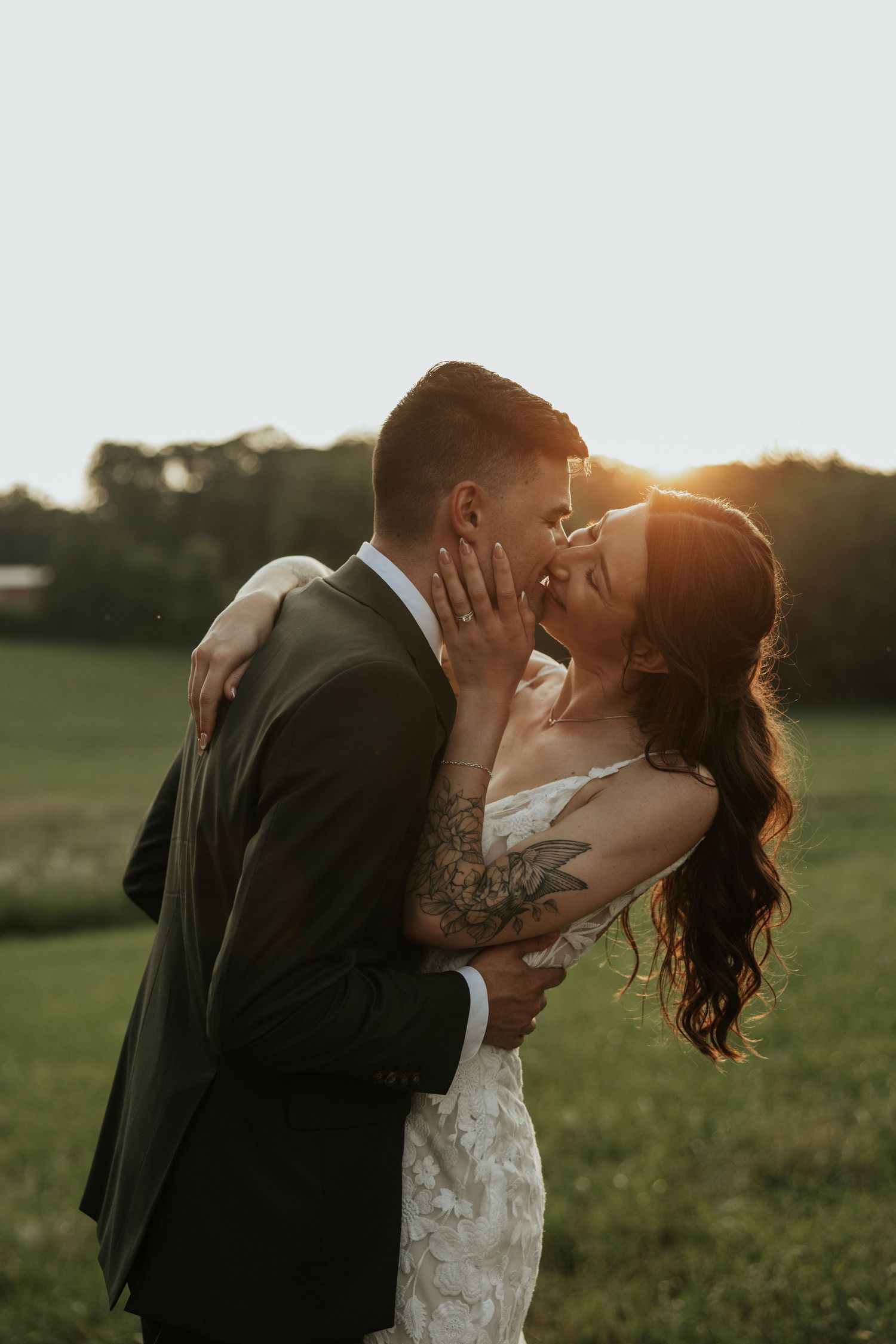 Newlywed couple sharing romantic kisses in a sunlit meadow at golden hour with natural landscapes in background.