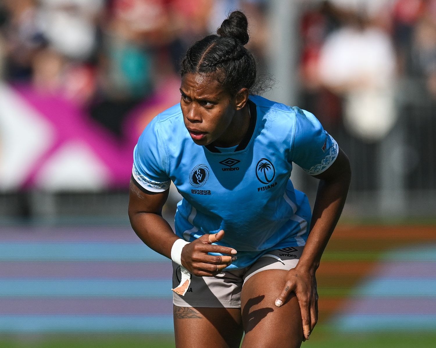 Track athlete wearing light blue uniform kneels down on racing track during athletic competition.