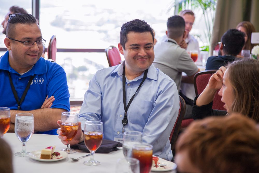 Professionals networking at a corporate lunch event, smiling and conversing at a dining table with drinks and desserts.