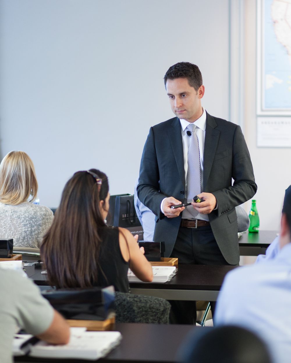Business professional in suit presenting to seated audience in modern conference room setting.