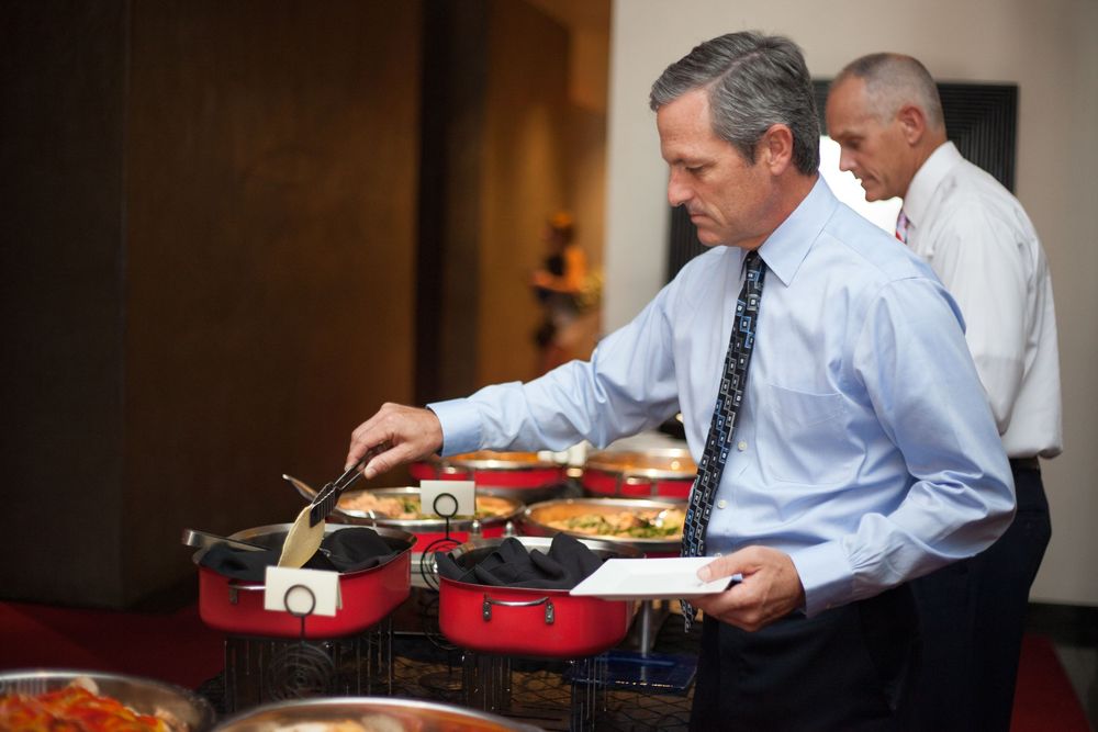 Business professionals eating at long tables during a catered event.