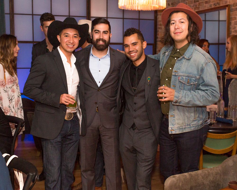 Four men smiling and posing together at an indoor social event, holding drinks in a stylish venue.