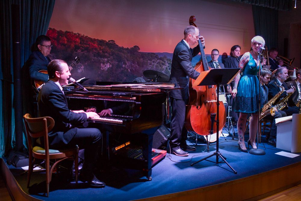 Jazz band performs live on stage with piano, double bass, saxophone, and vocalist in elegant blue dress at upscale venue.