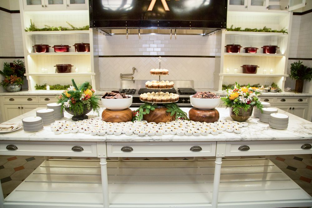 Elegant buffet table with tiered cake stand, floral arrangements, and assorted dishes in a bright white kitchen setting.