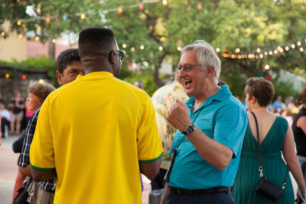 People mingle and socialize during an outdoor evening event with string lights.