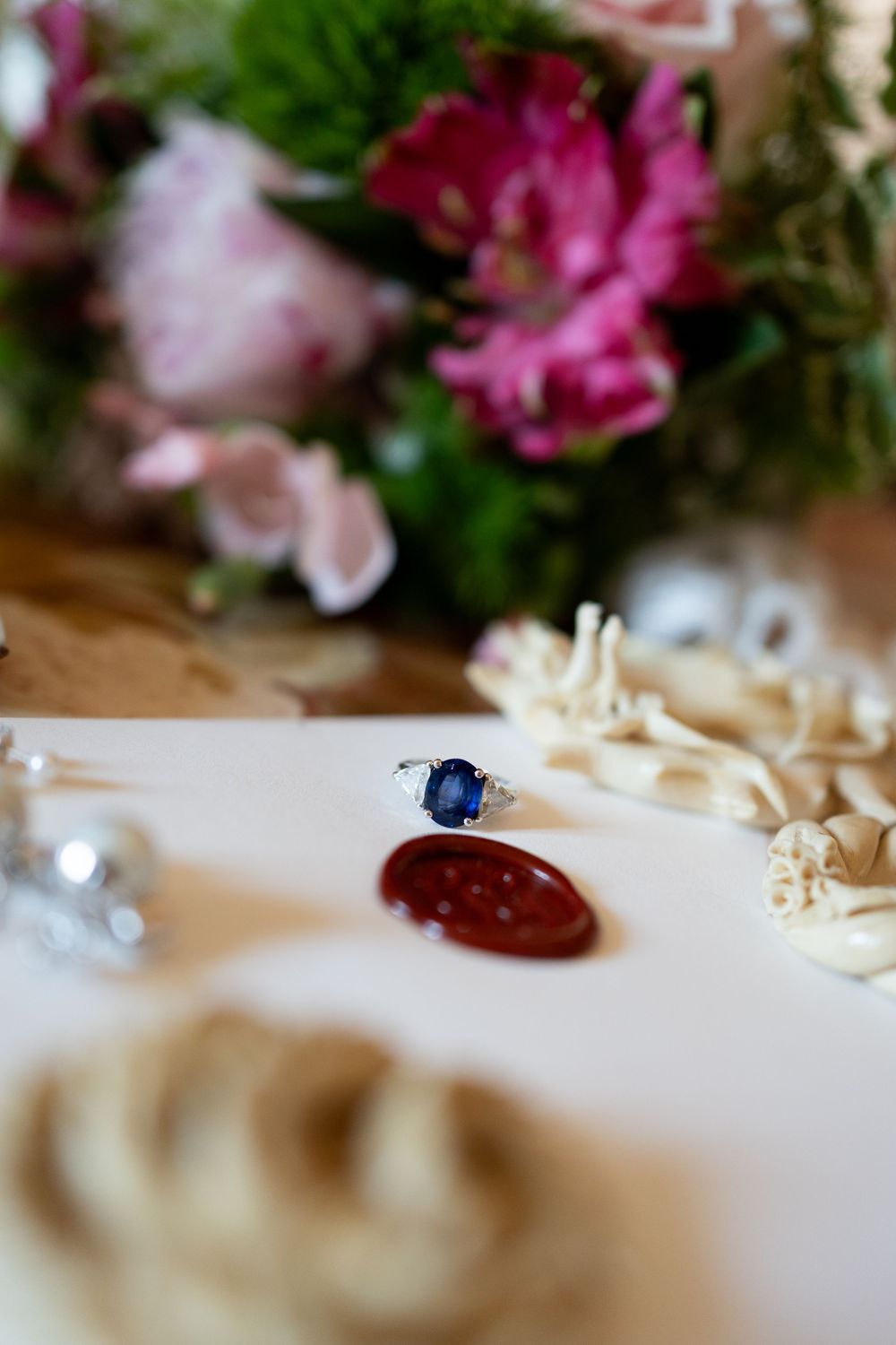 Close-up view of elegant jewelry and floral decorations on a light colored surface with pink flowers in soft focus.