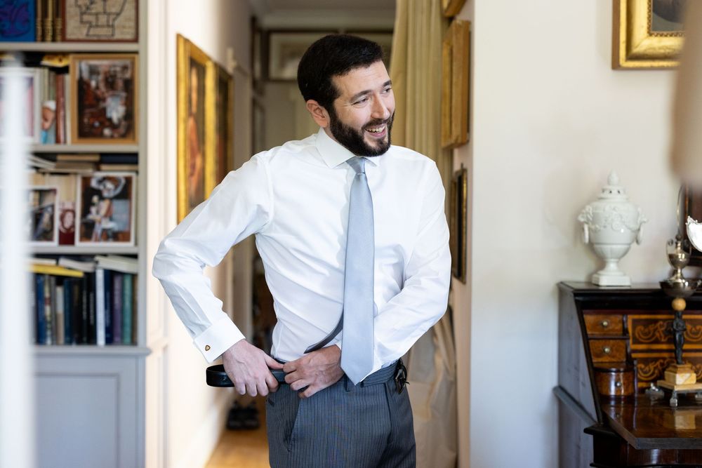 Professional in a white dress shirt and grey vest stands in an elegant room with framed artwork and decor.