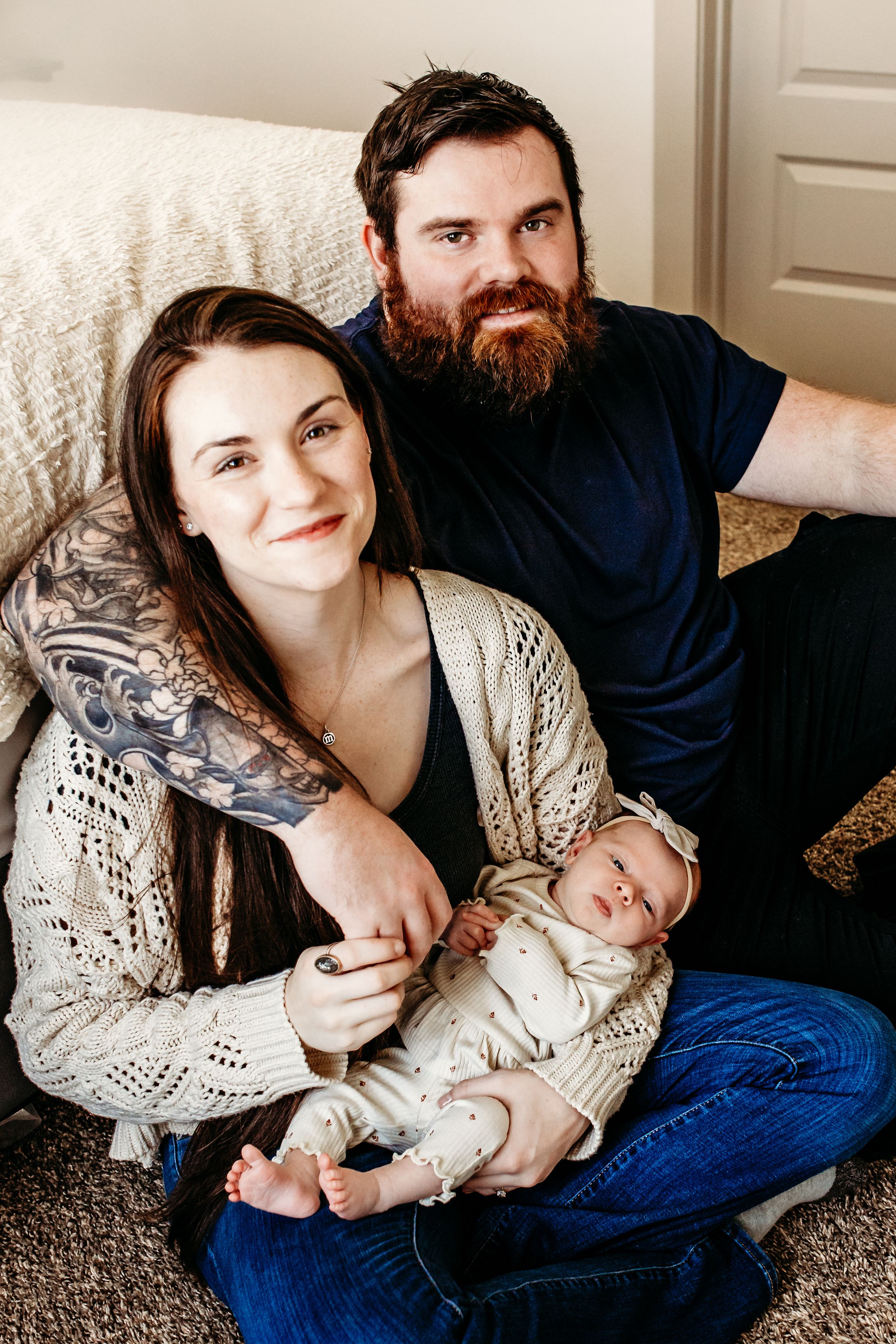 Couple sitting together on grey carpet wearing jeans and casual clothing in intimate lifestyle photoshoot setting.