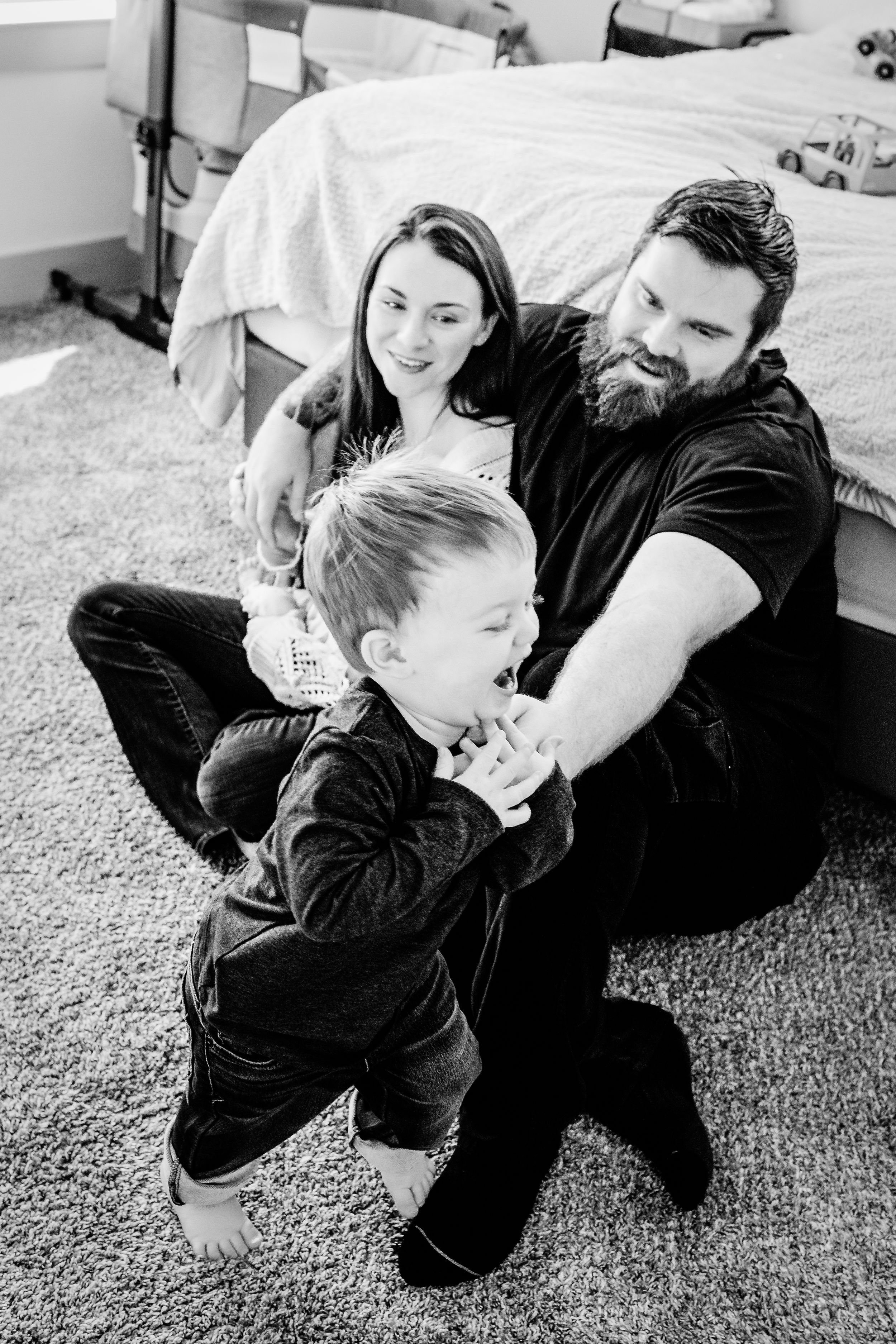 Playful black and white photo series showing gentle interactions between parent and child on carpeted floor.