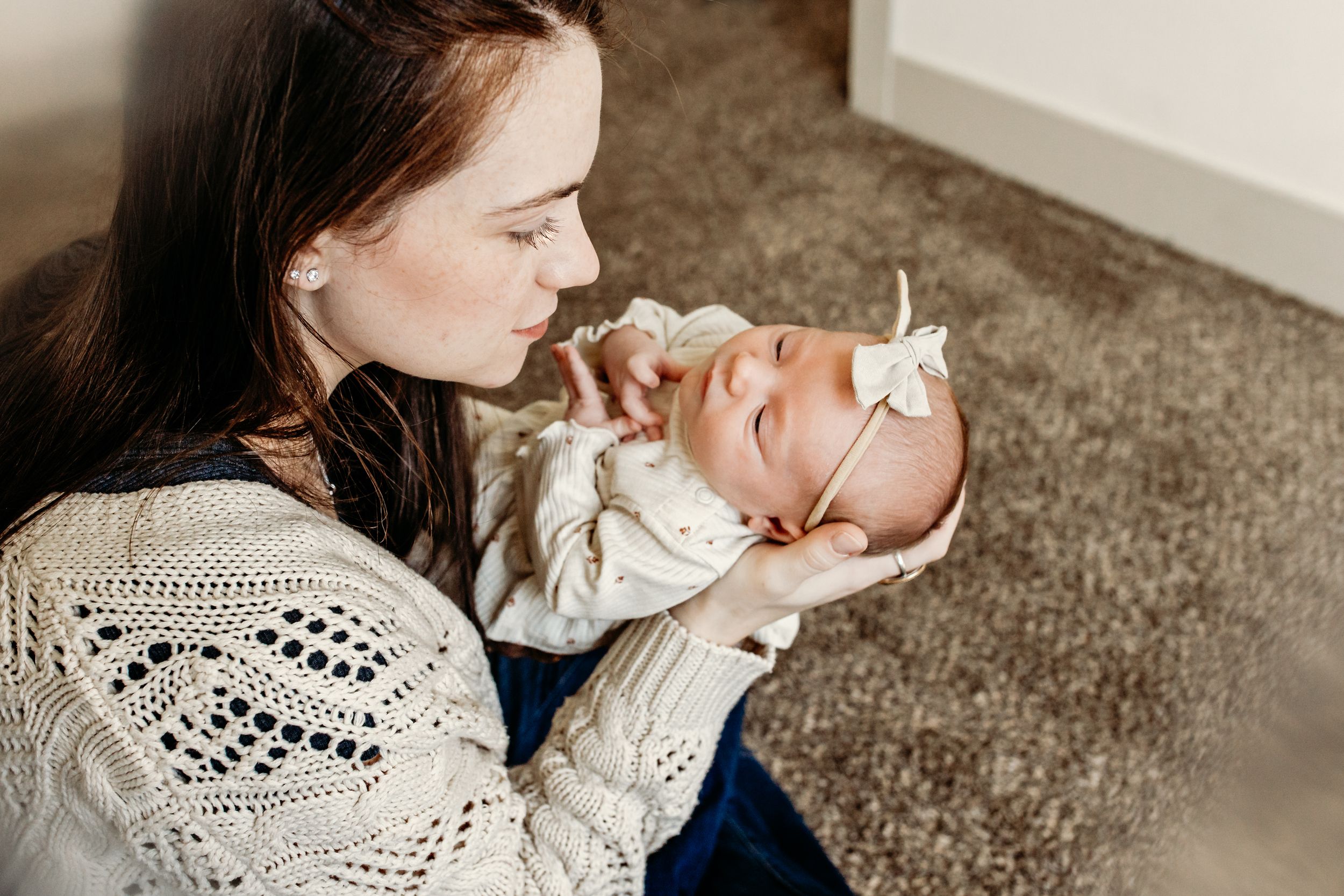Close-up view of a newborn baby being tenderly cradled in soft white knit clothing against a neutral background.