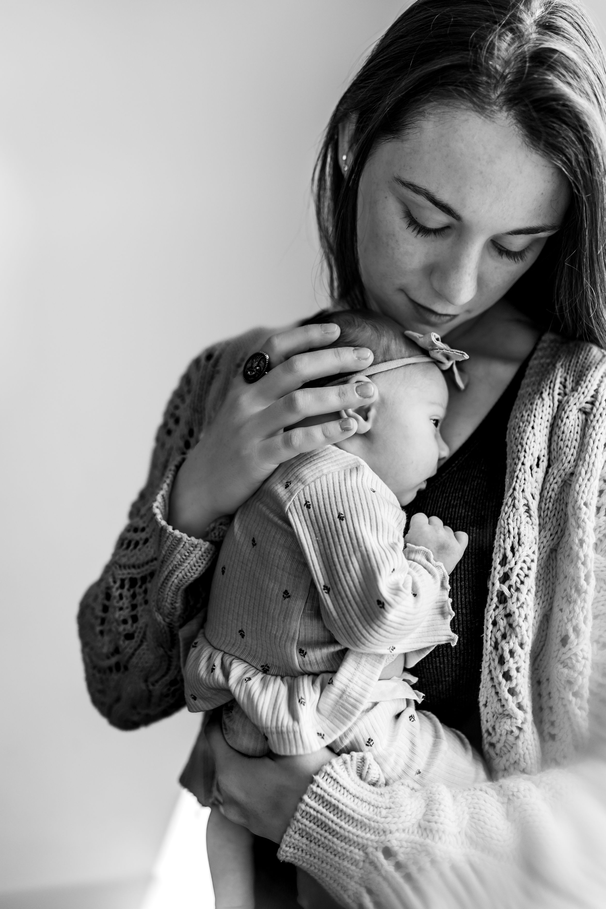 A tender black and white portrait showing a parent gently cradling their sleeping infant in knit sweaters.