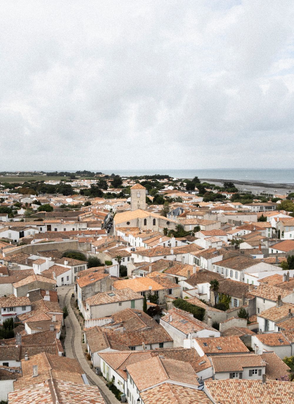 Panoramic aerial view of a Mediterranean coastal town with terracotta rooftops and whitewashed buildings sprawling toward the sea.