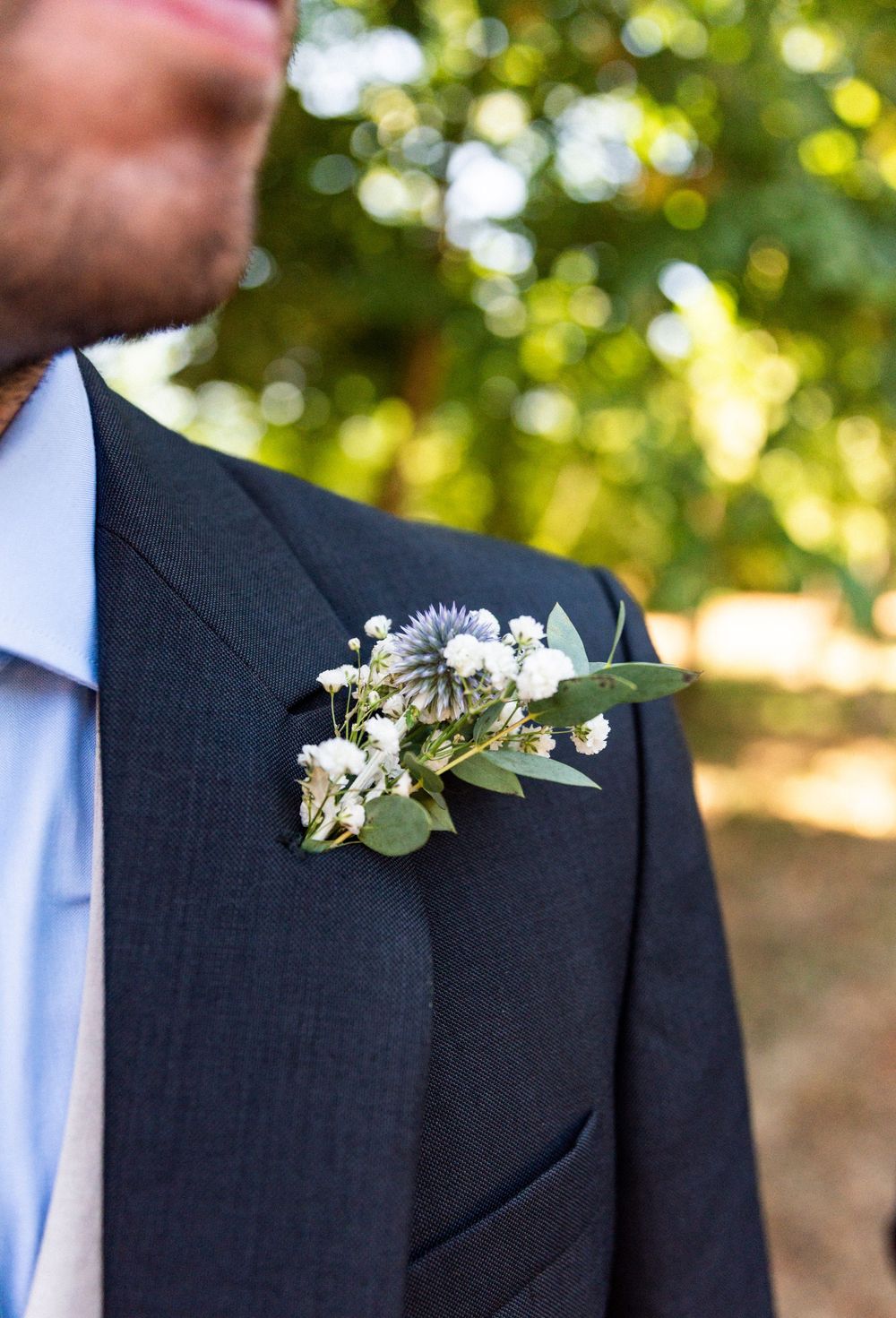 Close-up of groomsmen wearing black suits with delicate white floral boutonnieres against a soft bokeh background.