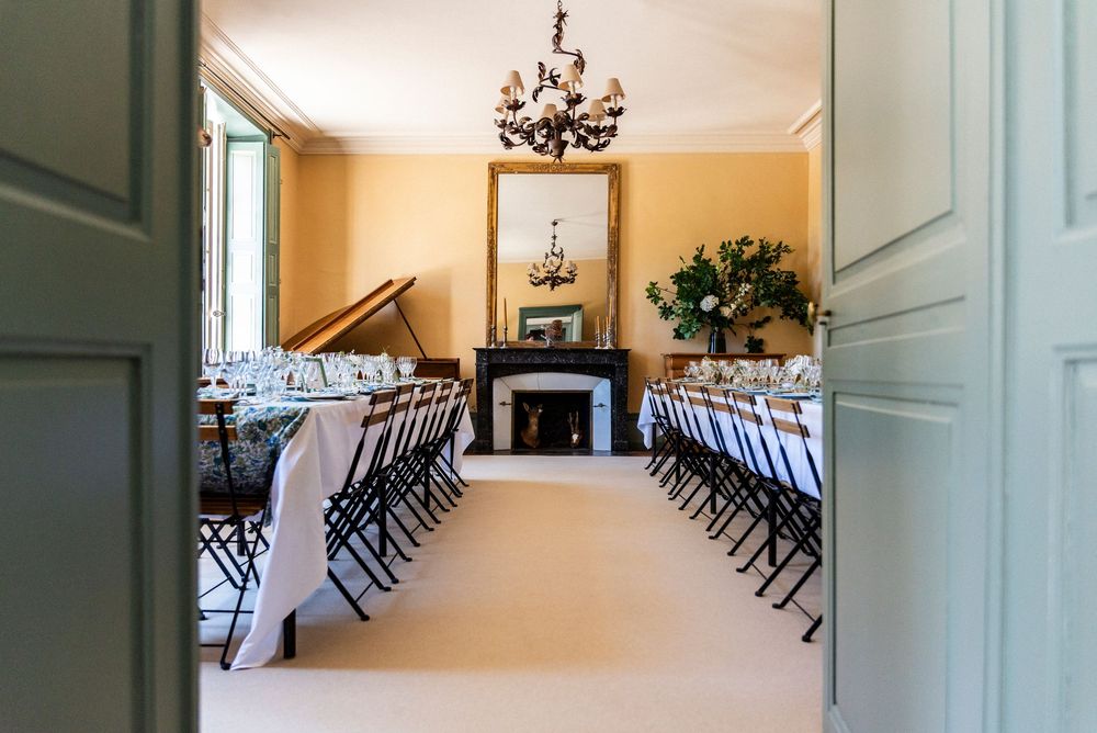 A long hallway with green double doors features a chandelier and rows of black folding chairs along the walls.