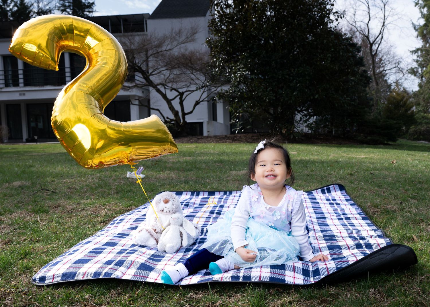 Large metallic gold number 2 balloon stands out against a natural outdoor setting with trees and grass in the background.