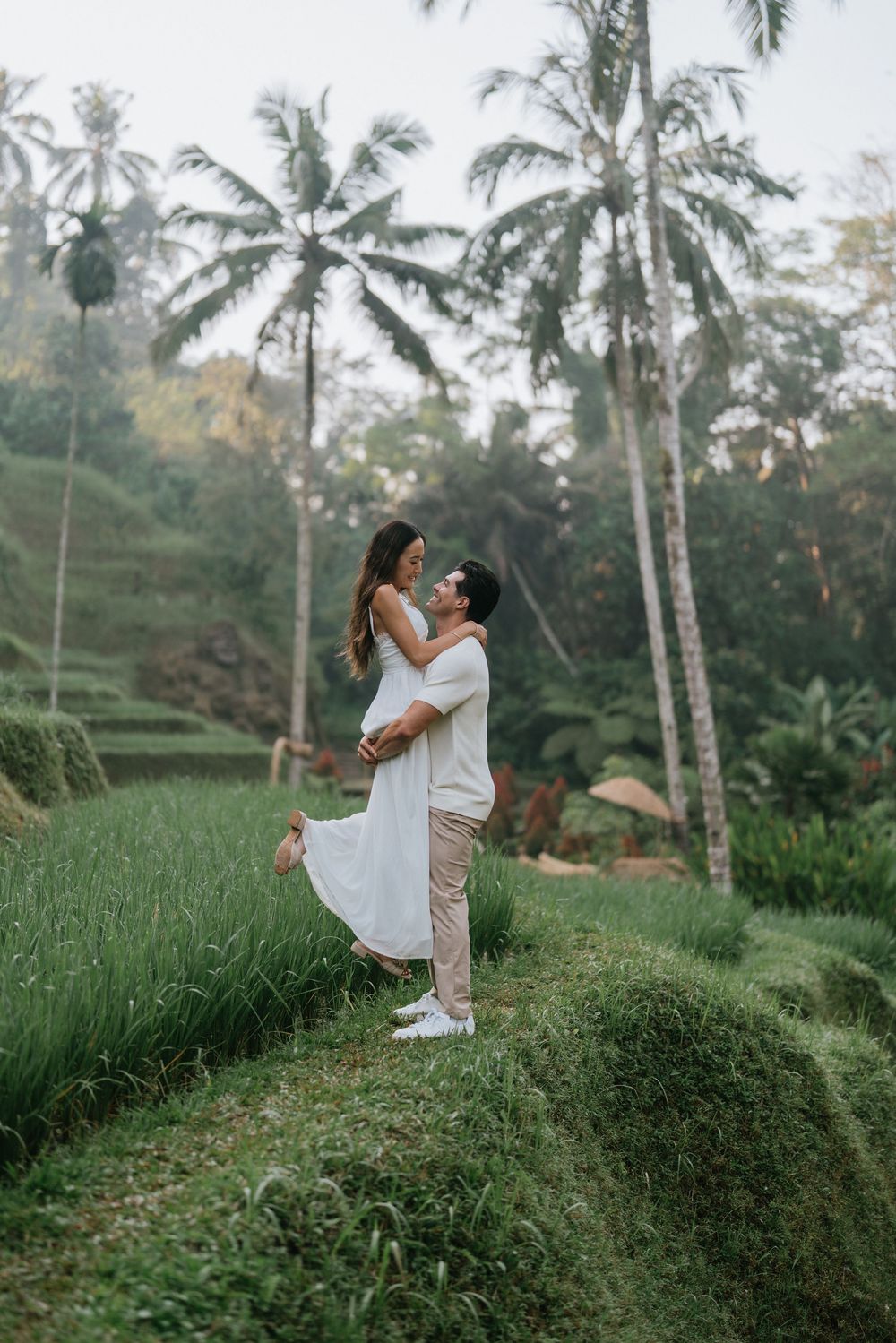 A romantic couple embracing on terraced rice fields with palm trees in Bali at sunset.