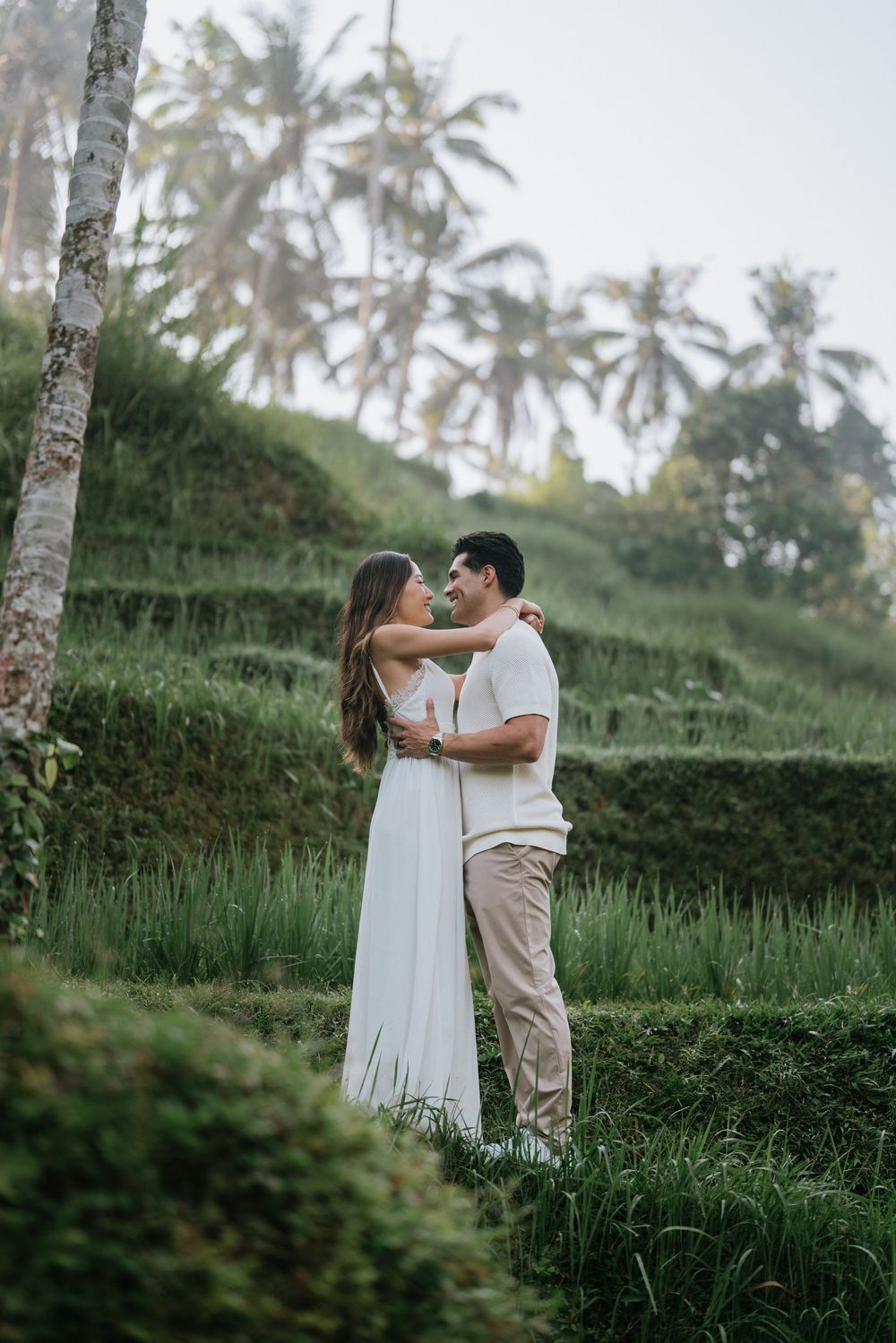 A couple sharing a romantic moment on green terraced rice fields with palm trees in the background.