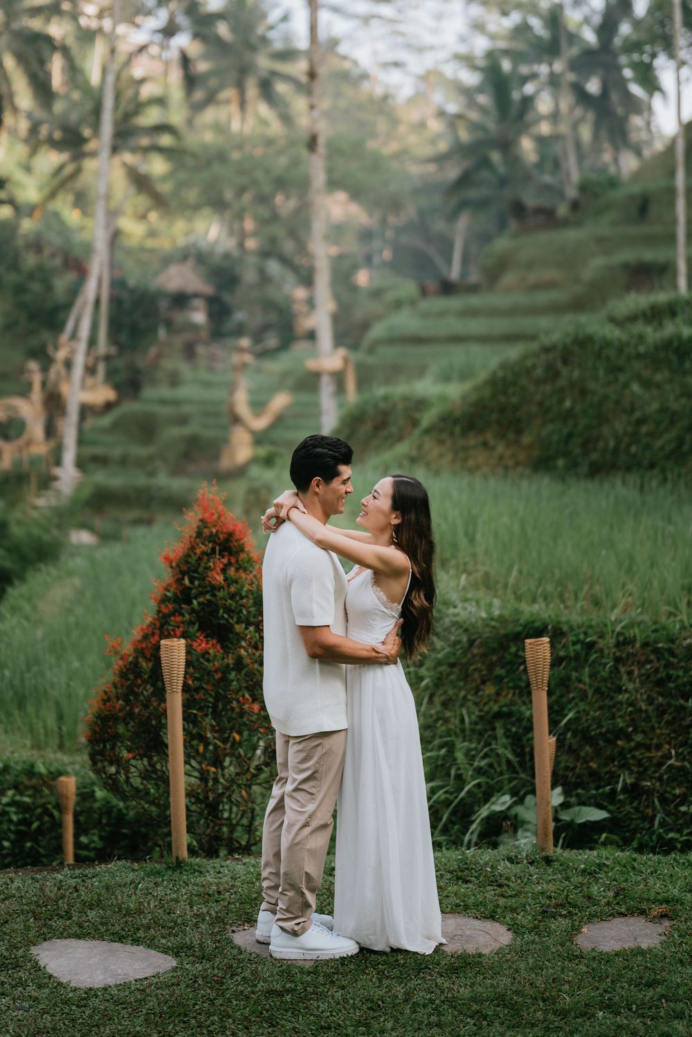 A couple embracing on a manicured path surrounded by tropical landscaping and rice terraces.