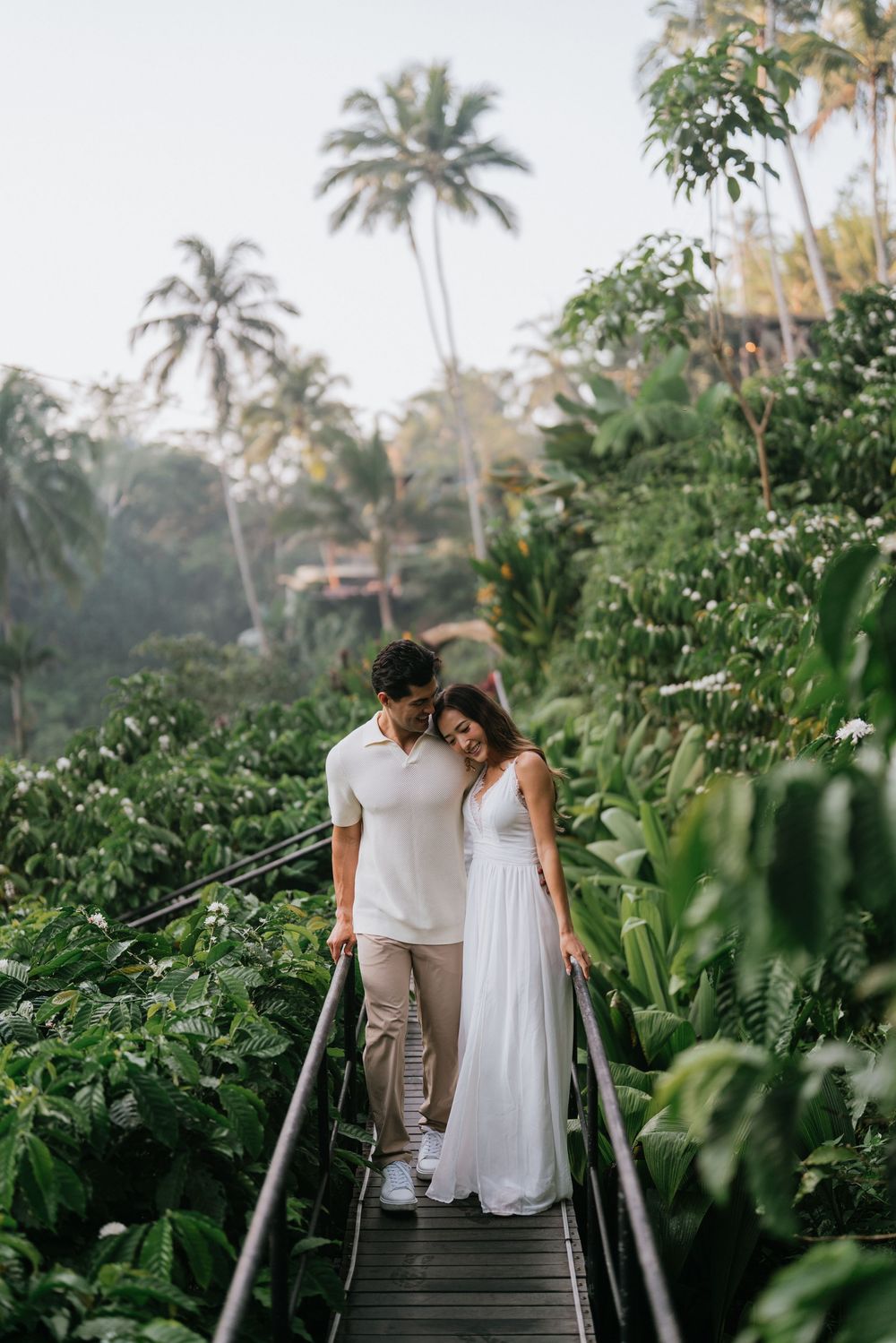 Couple descends stone steps surrounded by lush tropical garden and palm trees.