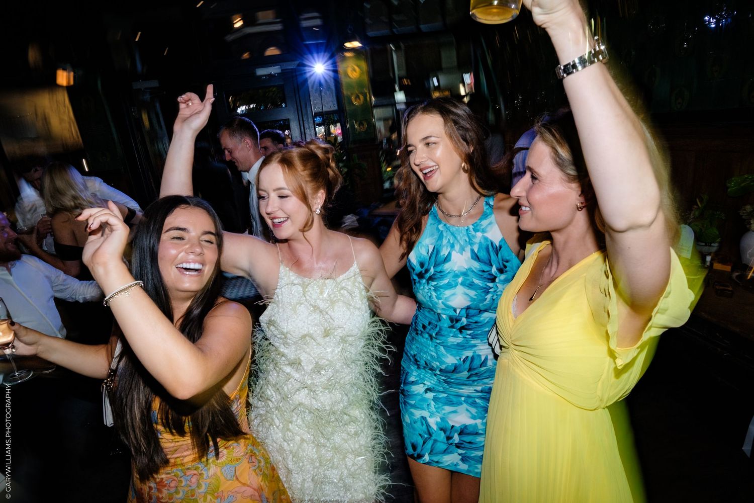 People dancing and celebrating at a lively nighttime party wearing colorful dresses in white, blue and yellow.
